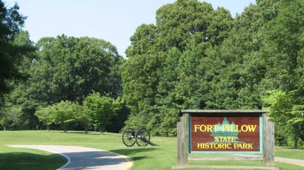 Road with a Civil War cannon and sign reading "Fort Pillow State Park" off to the side. Trees in background