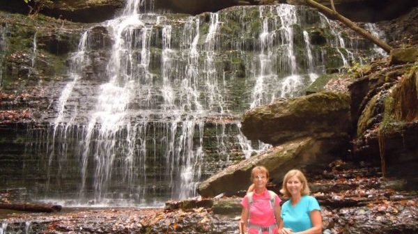 Waterfall with 3 levels in wooded area with 2 hikers in front
