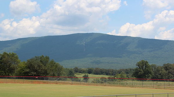 Mowed field in front with large green mountain ridge in the background with partly cloudy blue sky