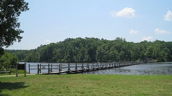 Wooden pedestrian bridge across a lake with green lawn and woods